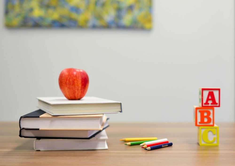 A stack of books on a table with an apple on top.